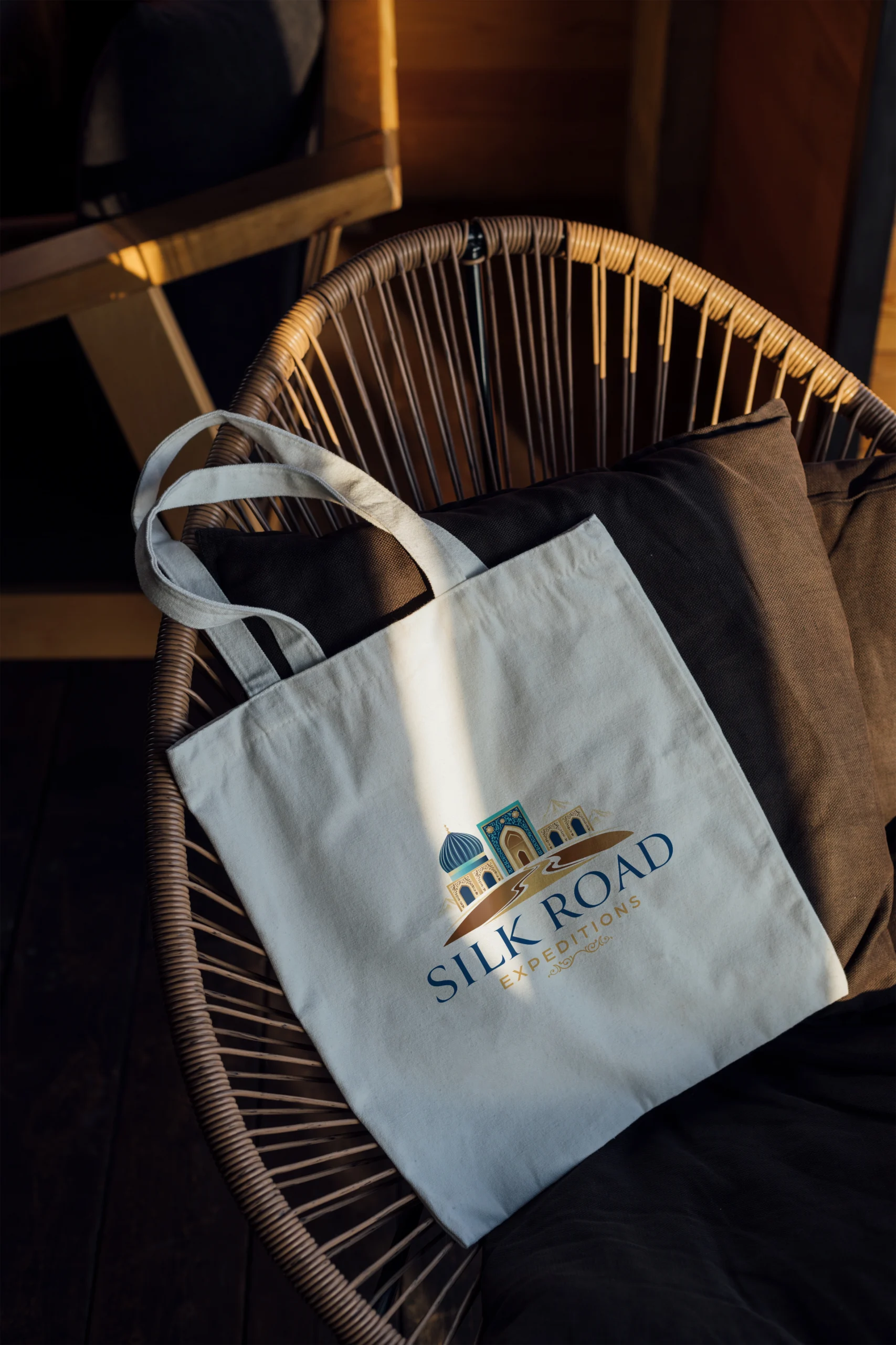 Weiße Stofftasche mit Silk Road Expeditions Logo auf Korbstuhl – Merchandise Branding Mockup